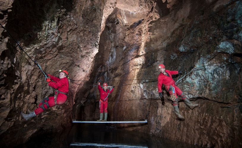 3 people wearing red wetsuits climbing caves
